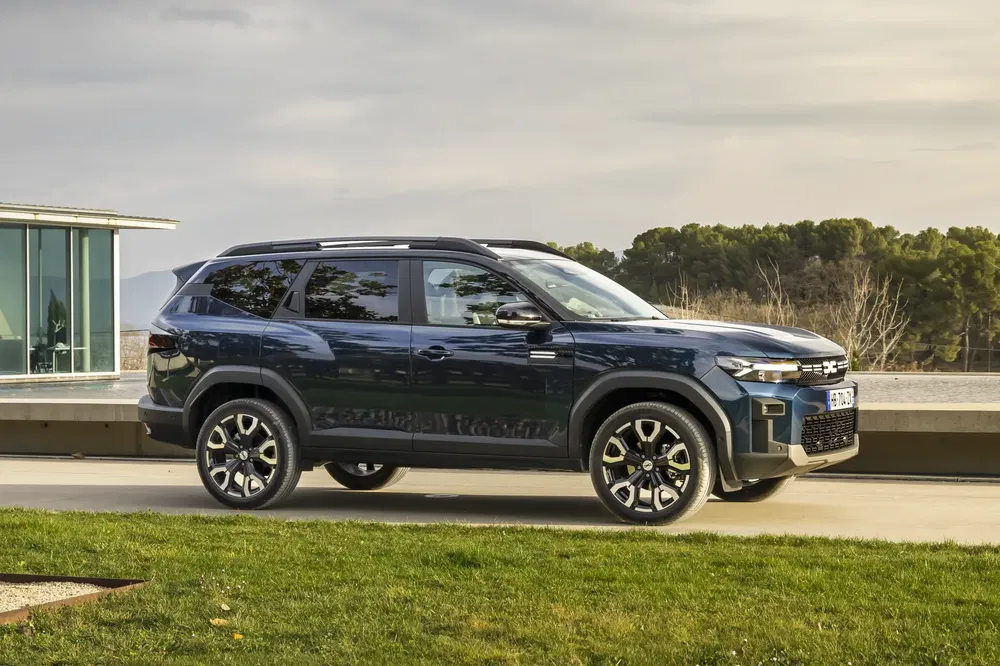 SUV Dacia Duster 2024 garé devant un bâtiment moderne sous un ciel nuageux.