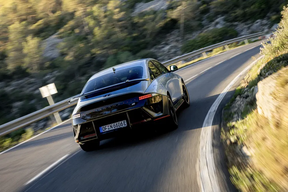 Hyundai Ioniq 6 sur route sinueuse, arrière du véhicule, paysage boisé.