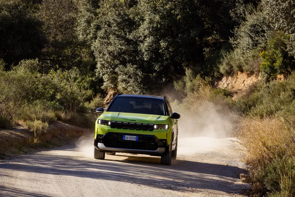 Groene Jeep Avenger op stoffige weg omringd door weelderig groen.