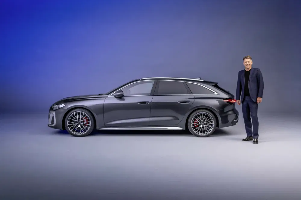 Grijze Audi A6 Avant e-tron met man in pak ernaast tegen een blauwe achtergrond.