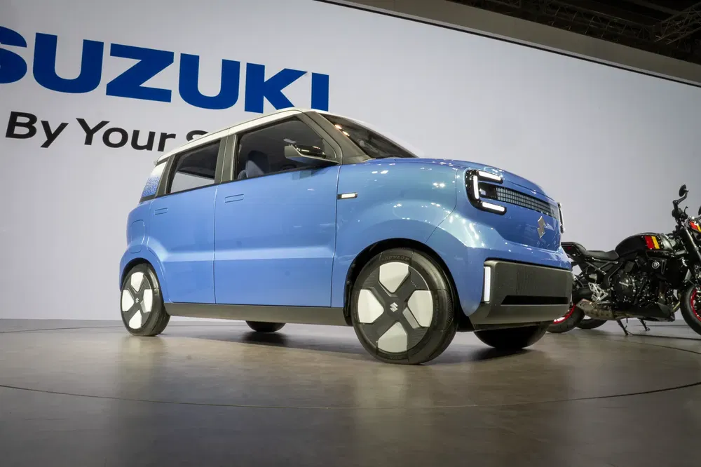 Blauwe elektrische conceptauto van Suzuki tentoongesteld met motorfiets op een autosalon.