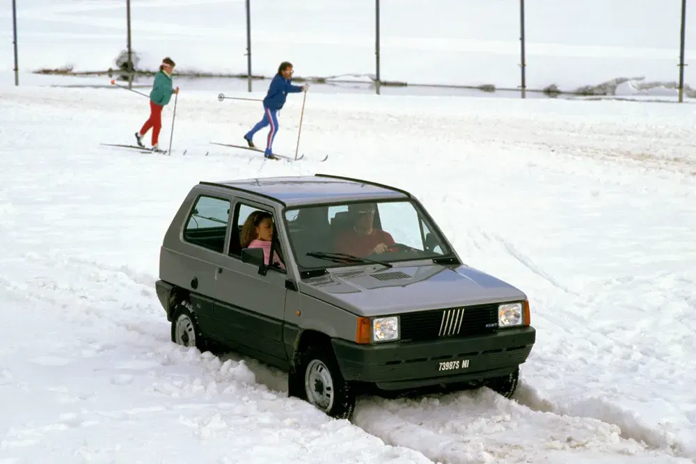 Fiat Panda rijdt door sneeuw met skiërs op de achtergrond.
