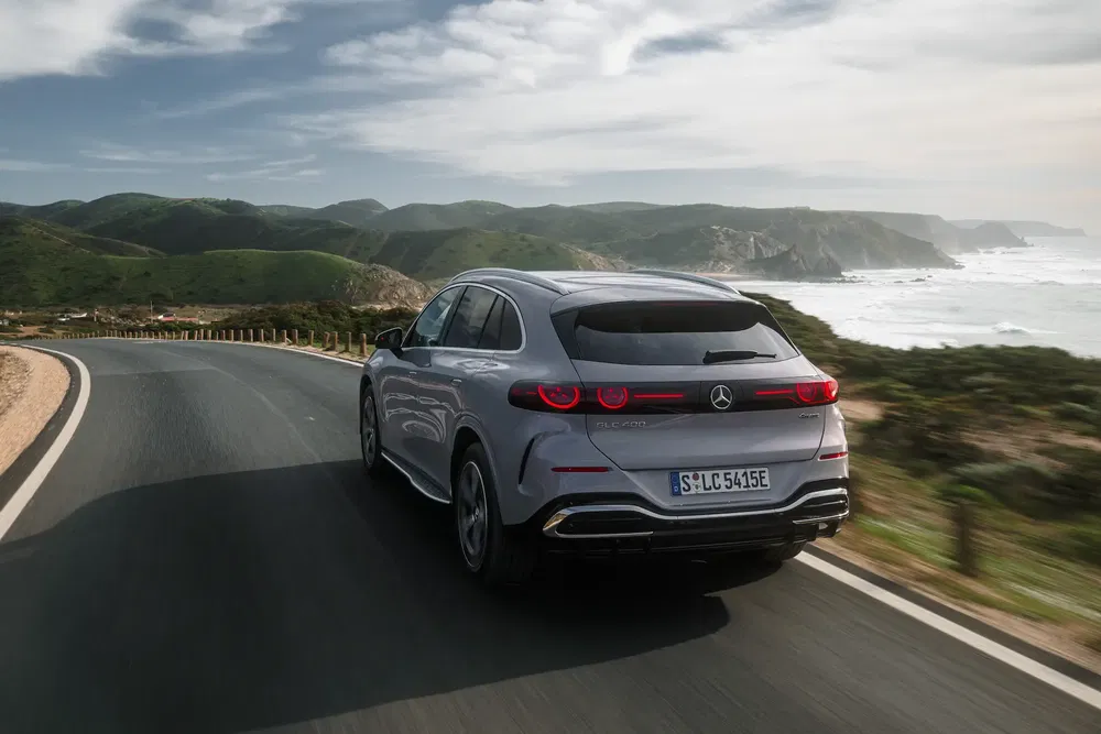 SUV Mercedes-EQ en route côtière avec vue sur l'océan et montagnes verdoyantes.