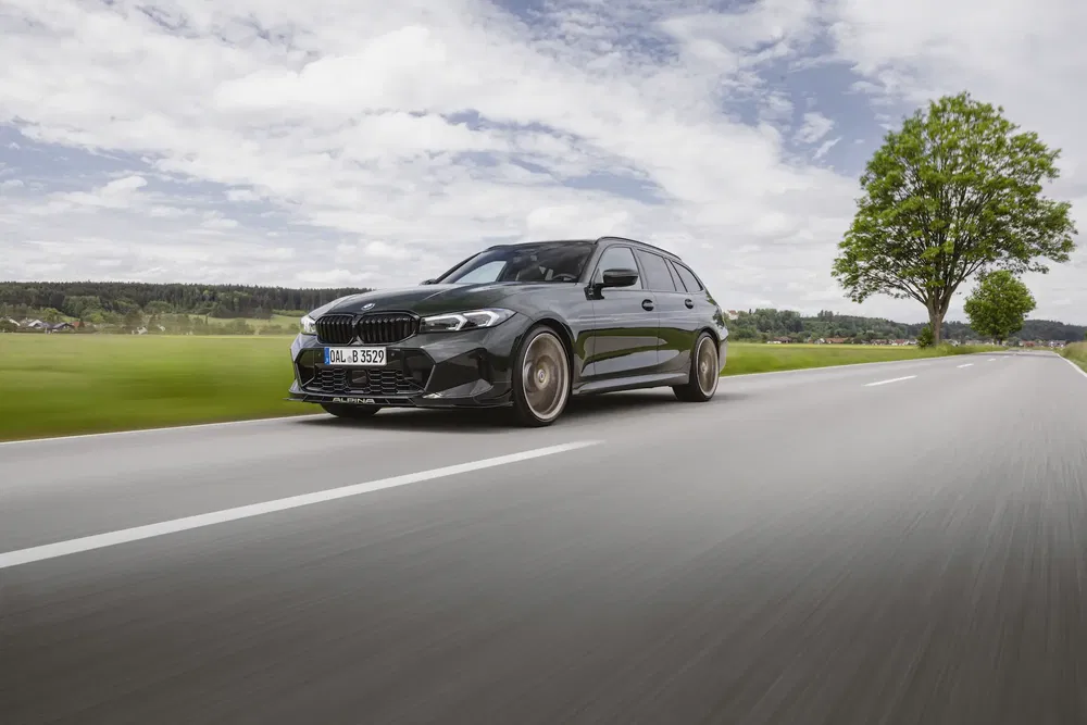 BMW Alpina B3 passe sur une route de campagne bordée d'arbres.