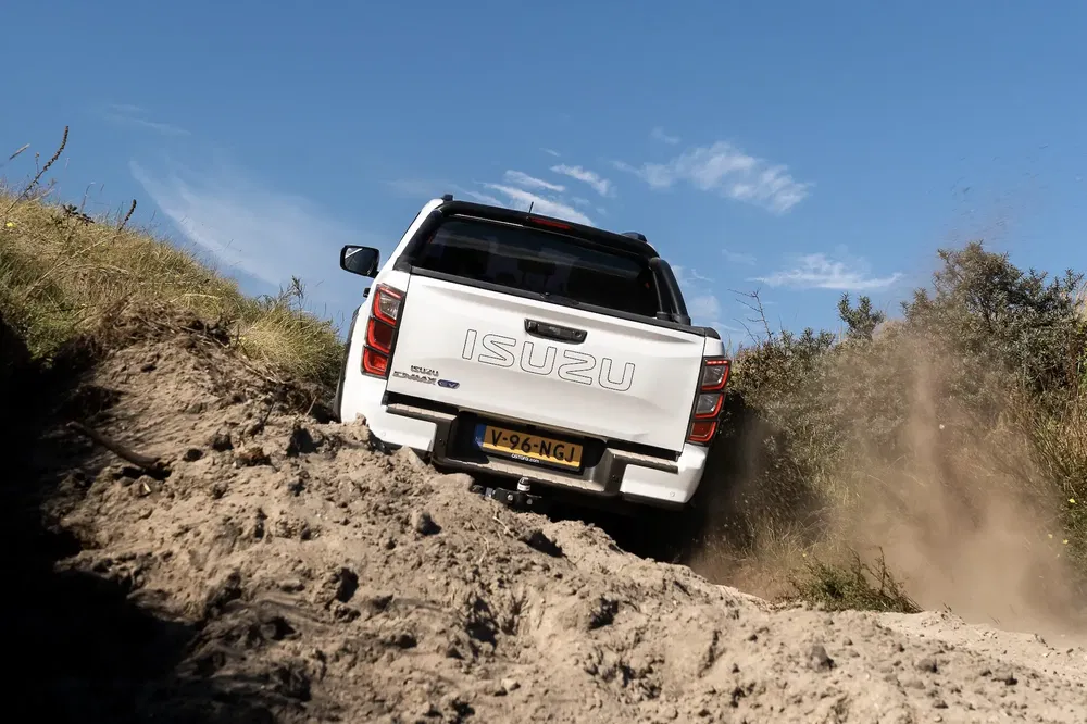 Isuzu D-Max blanc en conduite tout-terrain sur chemin sablonneux sous ciel bleu.