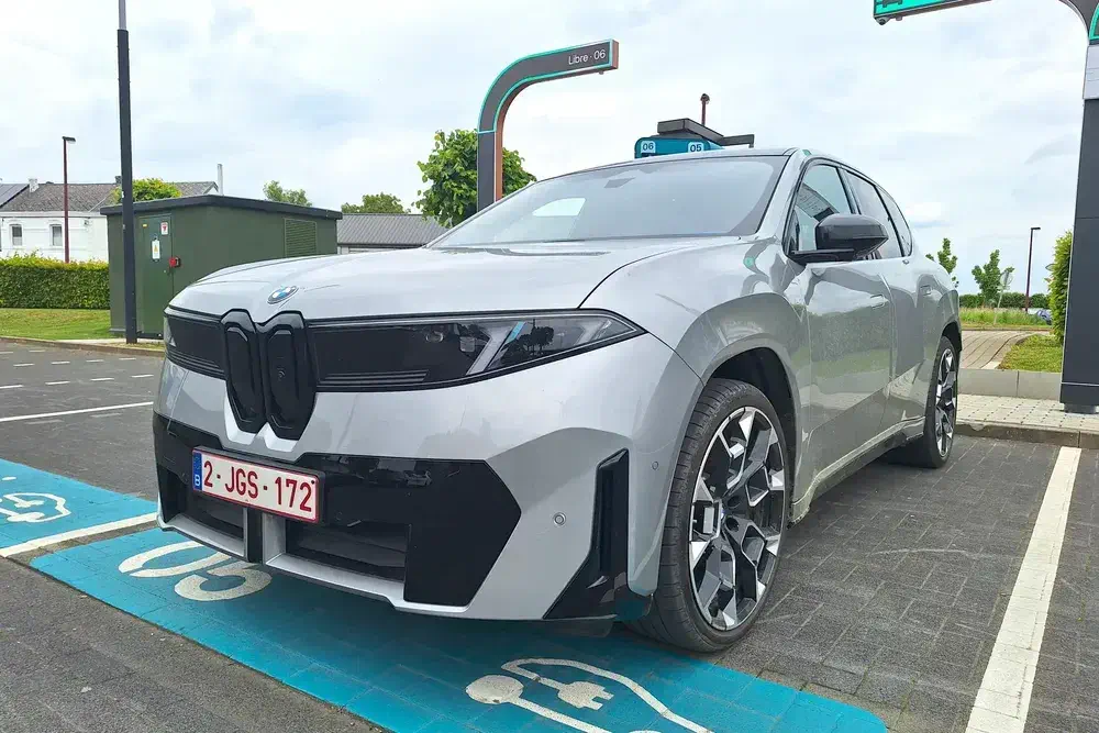BMW iX gris chargé sur borne électrique dans un parking urbain.