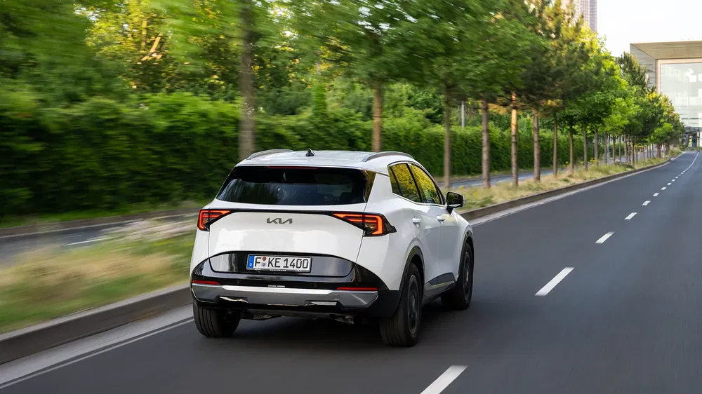 Kia Sportage blanche roulant sur une route bordée d'arbres, design moderne et élégant.