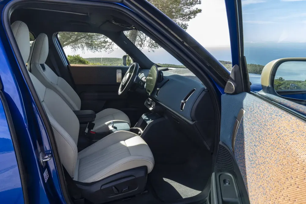 Intérieur d'une Mini Cooper SE bleu, avec sièges en cuir blanc, vue océanique.