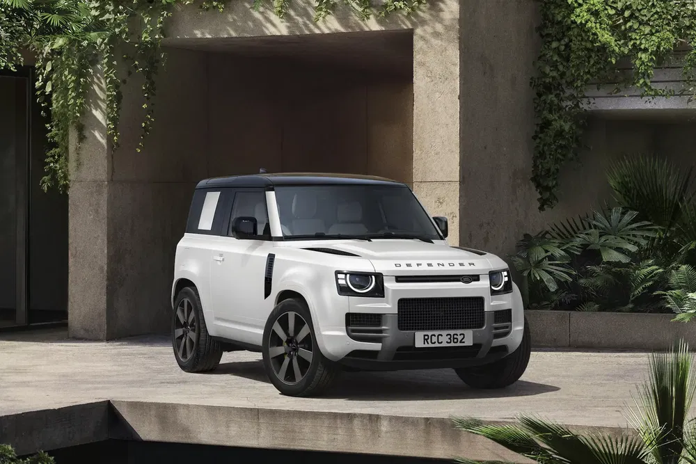 Land Rover Defender blanc garé devant un bâtiment moderne avec végétation luxuriante.