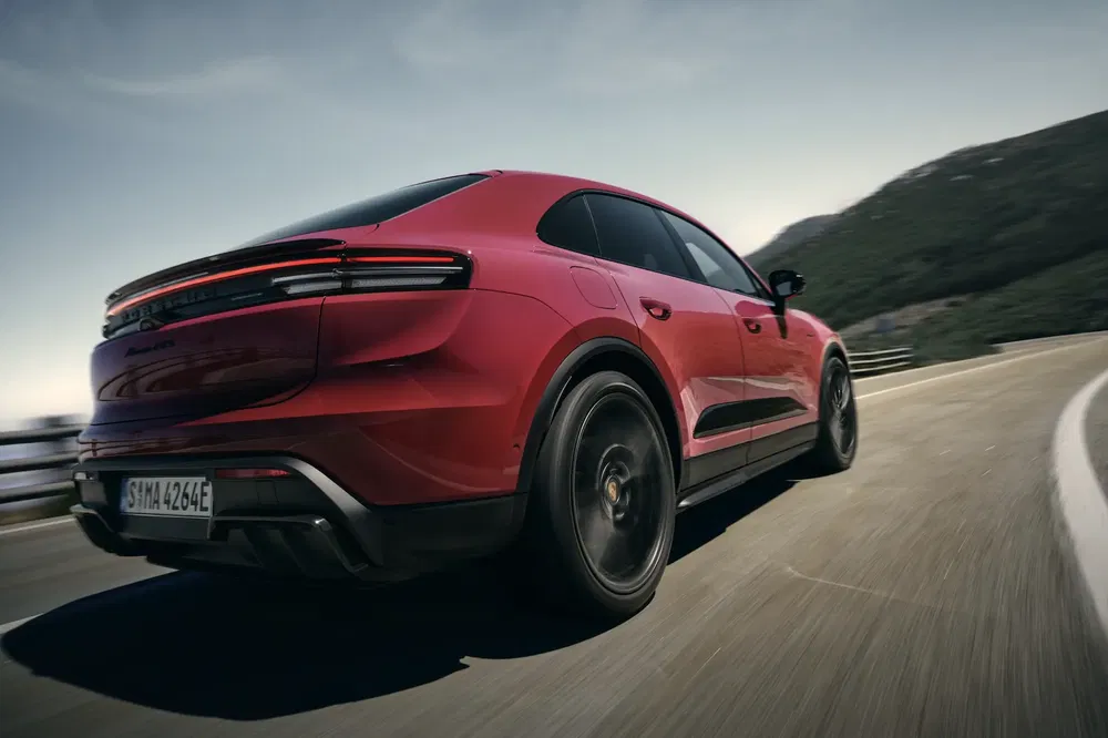 Porsche Cayenne rouge en virage serré sur route de montagne, profil arrière dynamique.