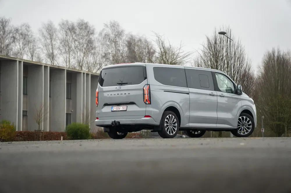 Ford Transit Custom gris stationné devant un bâtiment moderne par temps nuageux.