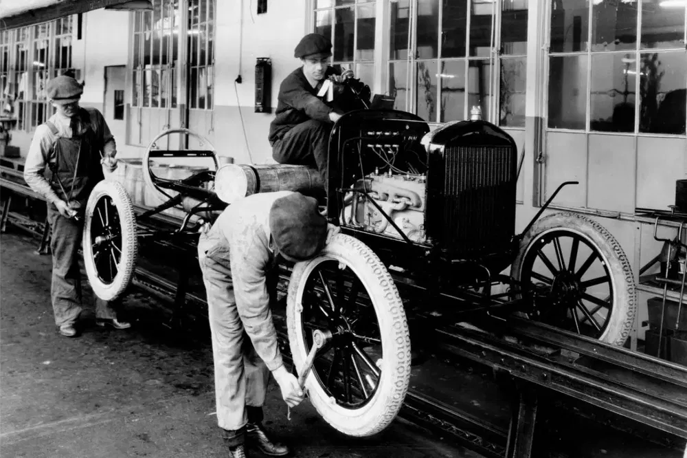 Atelier de montage d'une voiture Ford Model T en 1920, ouvriers ajustant les roues.