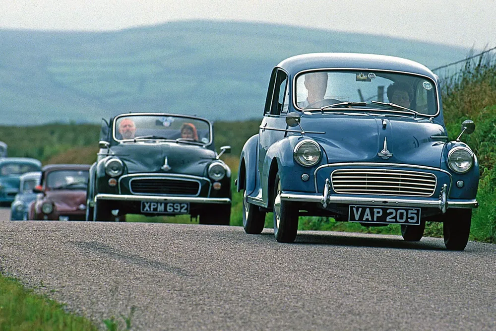 Convoi de voitures classiques Morris Minor sur une route de campagne pittoresque.