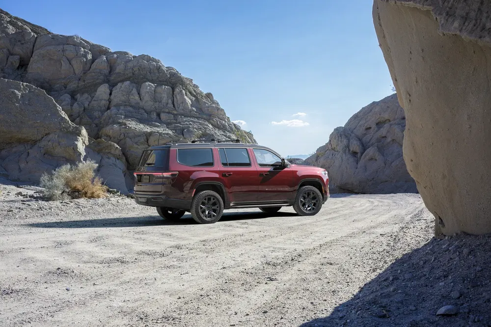 SUV rouge dans un désert rocheux sous un ciel bleu clair.