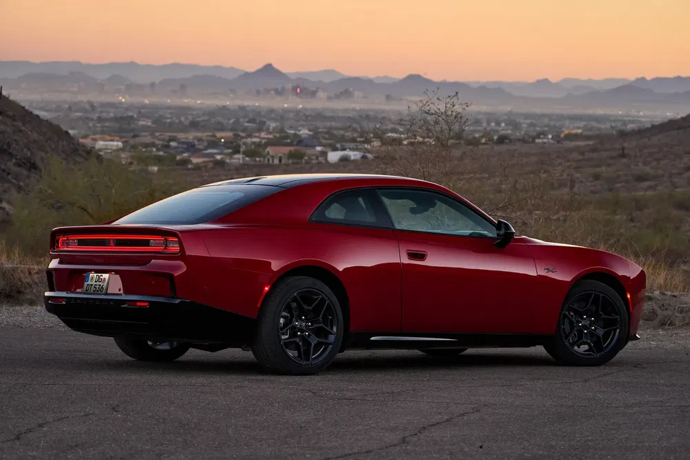 Dodge Challenger rouge au crépuscule avec vue panoramique sur la ville en arrière-plan.