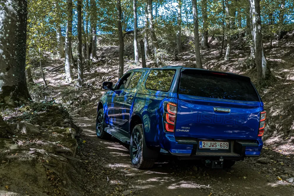 Isuzu D-Max bleu naviguant un chemin de forêt, démontrant sa capacité tout-terrain.