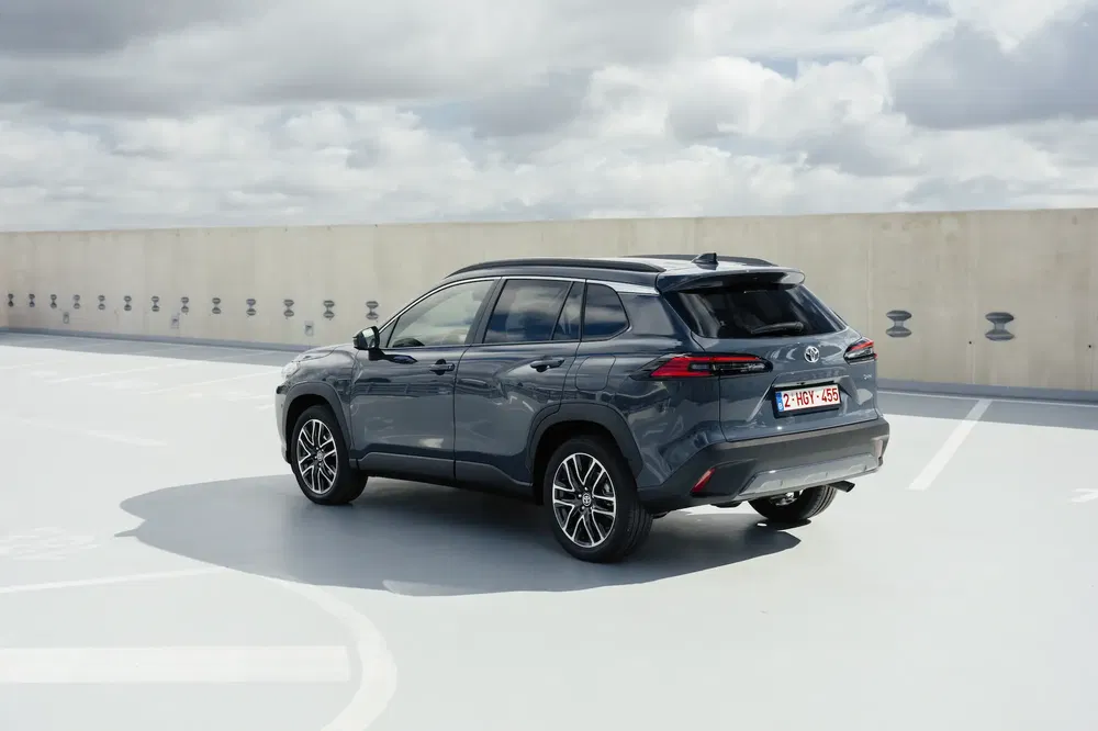 Toyota Corolla Cross gris sur un parking avec ciel nuageux en arrière-plan.