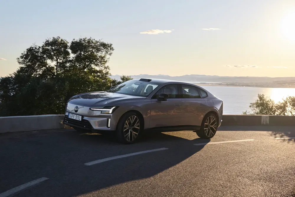 Voiture Polestar 2 grise se dirigeant vers le coucher de soleil, avec vue sur la mer.