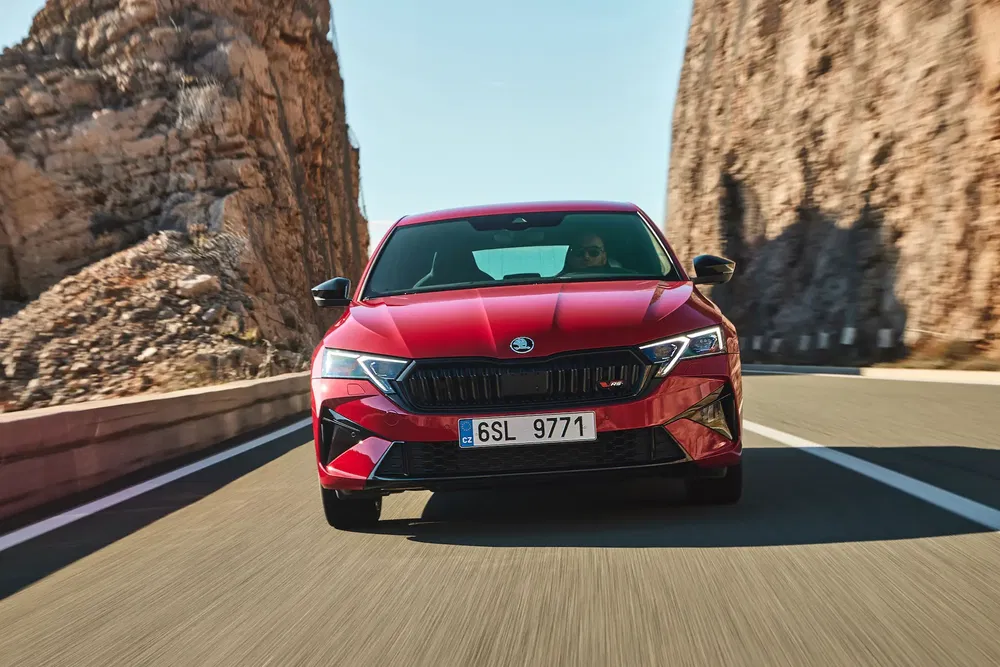 Skoda Octavia rouge roulant entre falaises, route déserte, ciel dégagé.