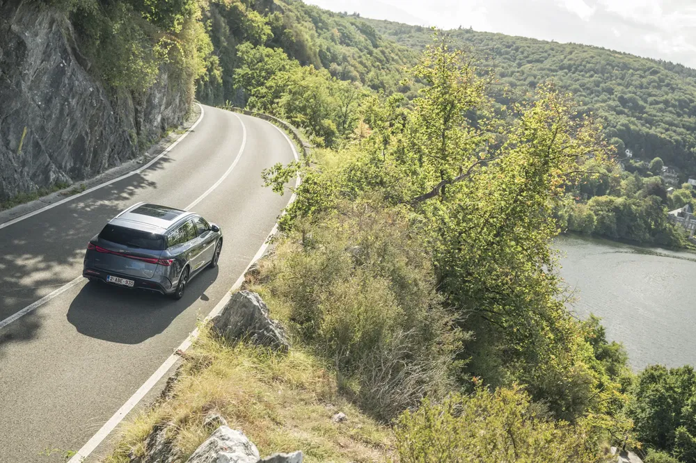 Voiture électrique sur route sinueuse bordée de forêts et réserve d'eau en montagne.