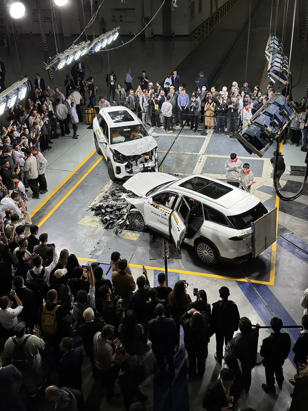 Botsproef met witte SUV onder toezicht van menigte in testfaciliteit.