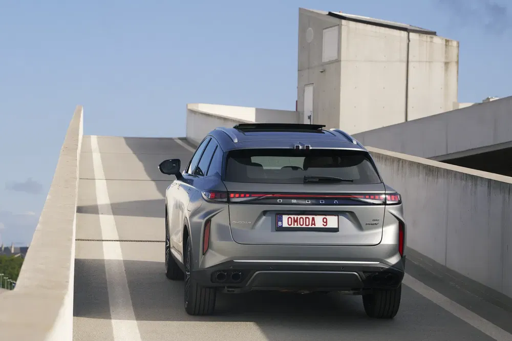Achteraanzicht van een grijze OMODA 9 SUV op een parkeerhelling.