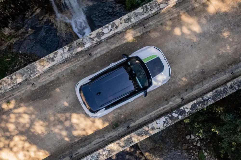 Vue aérienne d'une Abarth 500 électrique sur un pont en pierre, cascade en arrière-plan.