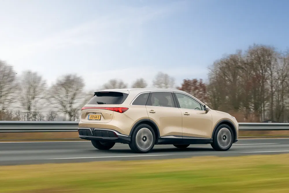 SUV MG Marvel R beige roulant sur autoroute, ciel bleu et arbres en arrière-plan.