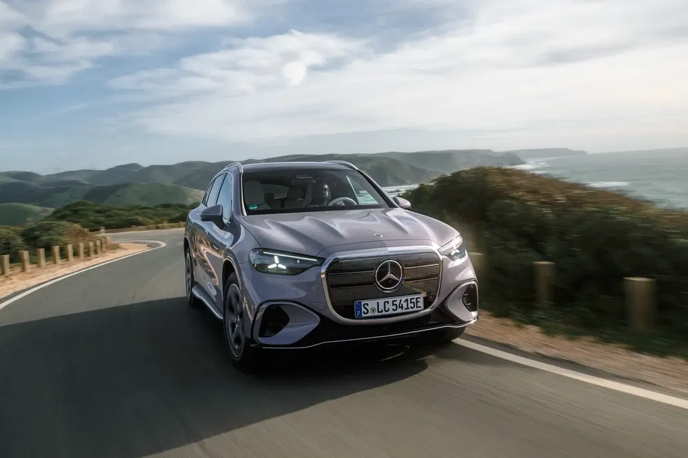 SUV Mercedes-Benz électrique roulant sur une route côtière, paysages verdoyants à l'horizon.