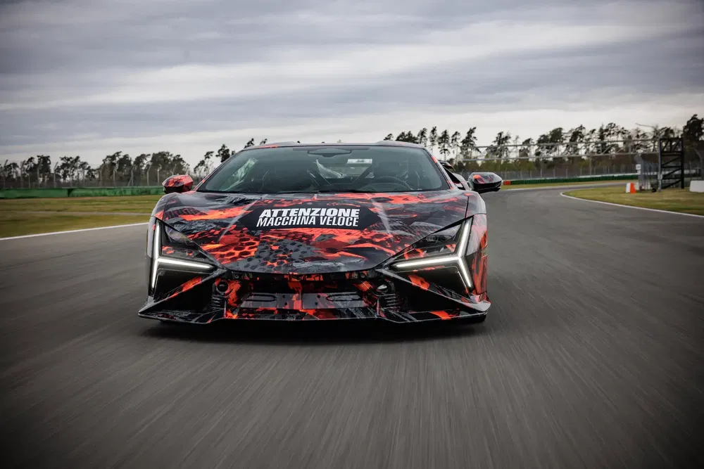Voiture de sport Lamborghini camouflée sur circuit, conduite rapide avec ciel couvert.