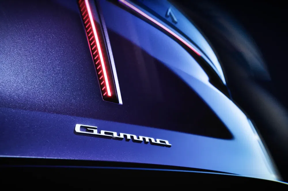 Vue rapprochée du logo 'Gamma' sur une voiture bleu foncé à la lumière LED rouge.