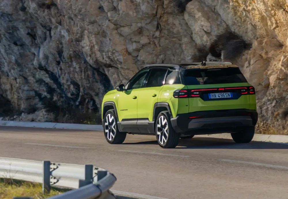 Felgroene Jeep op kronkelige weg, rotsachtige bergen op de achtergrond.