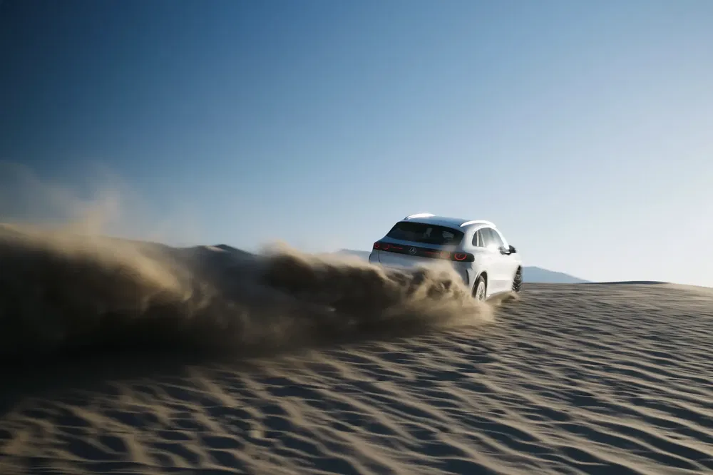 Voiture tout-terrain Bentley Bentayga dérive sur des dunes de sable sous ciel bleu clair.