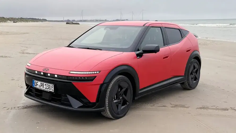 Hyundai Ioniq 5 rouge garée sur une plage, design moderne et futuriste sous ciel nuageux.
