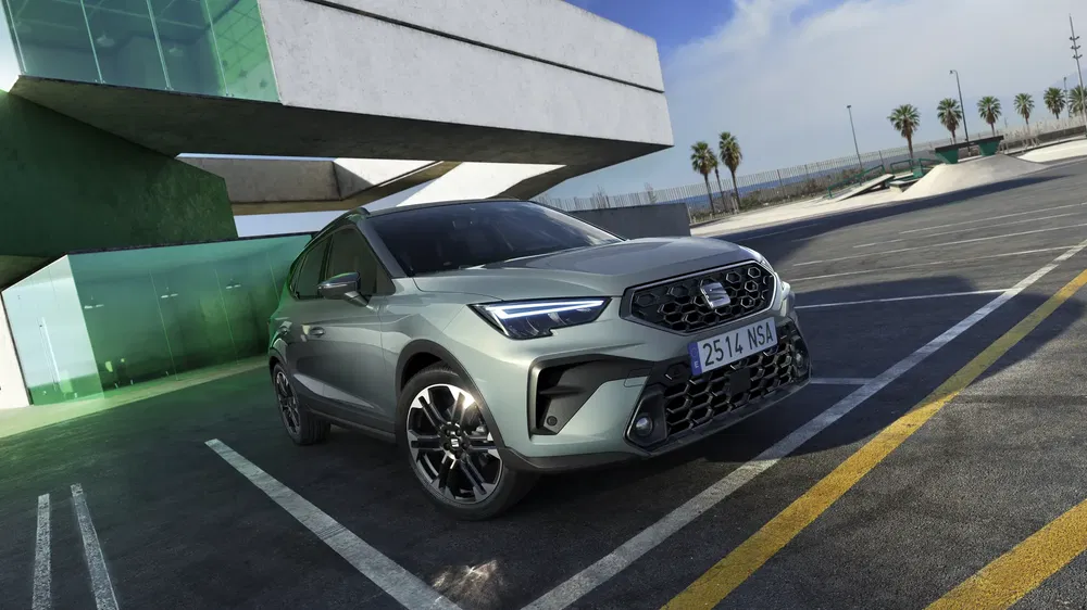 SUV Seat Arona gris garé devant un bâtiment moderne avec ciel dégagé.