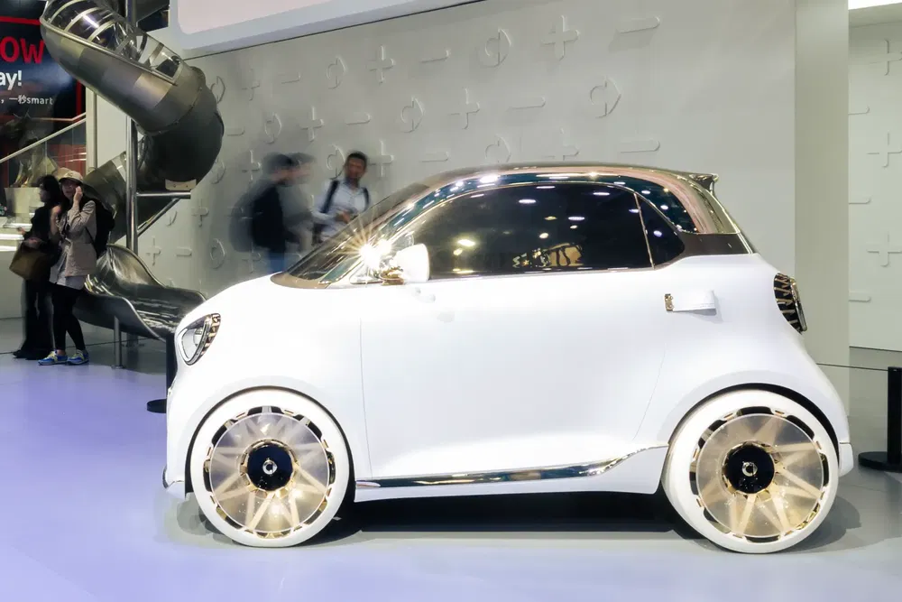 Concept-car électrique urbain blanc avec accents dorés exposé dans un salon automobile moderne.