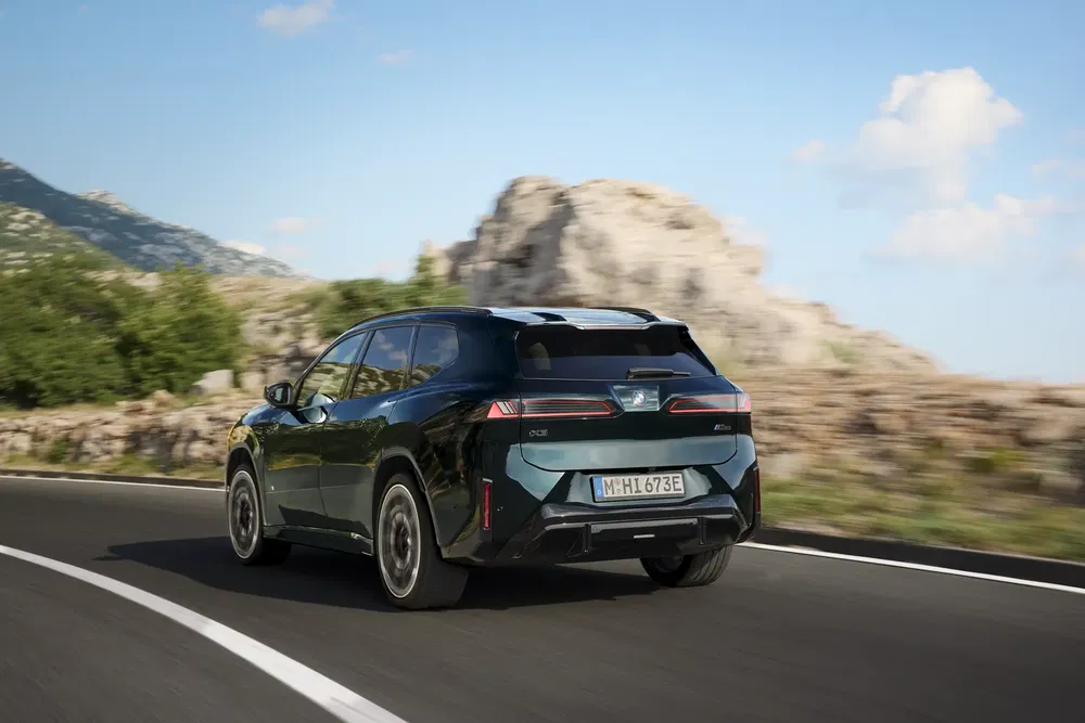 Le SUV électrique BMW iX en conduite sur route montagneuse sous ciel bleu et dégagé.