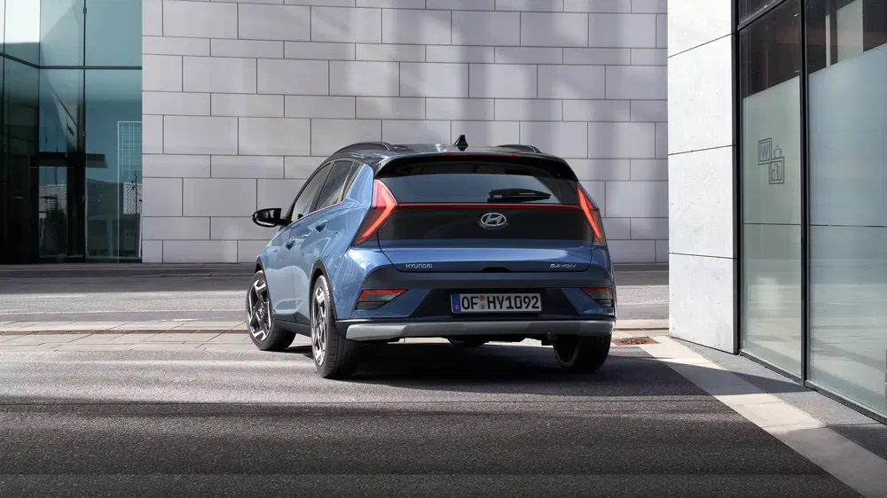 Hyundai i30 bleu garée, vue arrière, près d'un bâtiment moderne vitré.