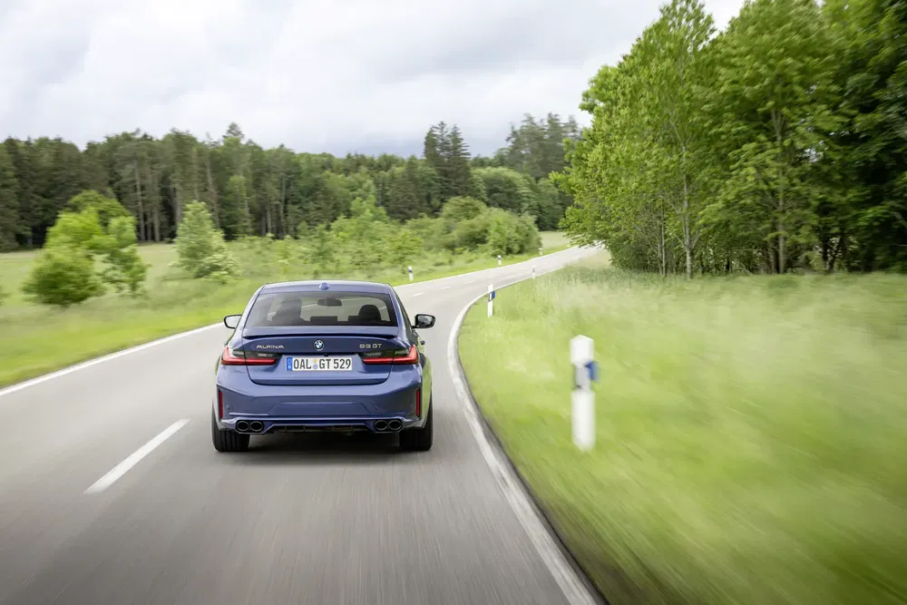 BMW Alpina B3 roulant sur une route de campagne sinueuse entourée de verdure luxuriante.