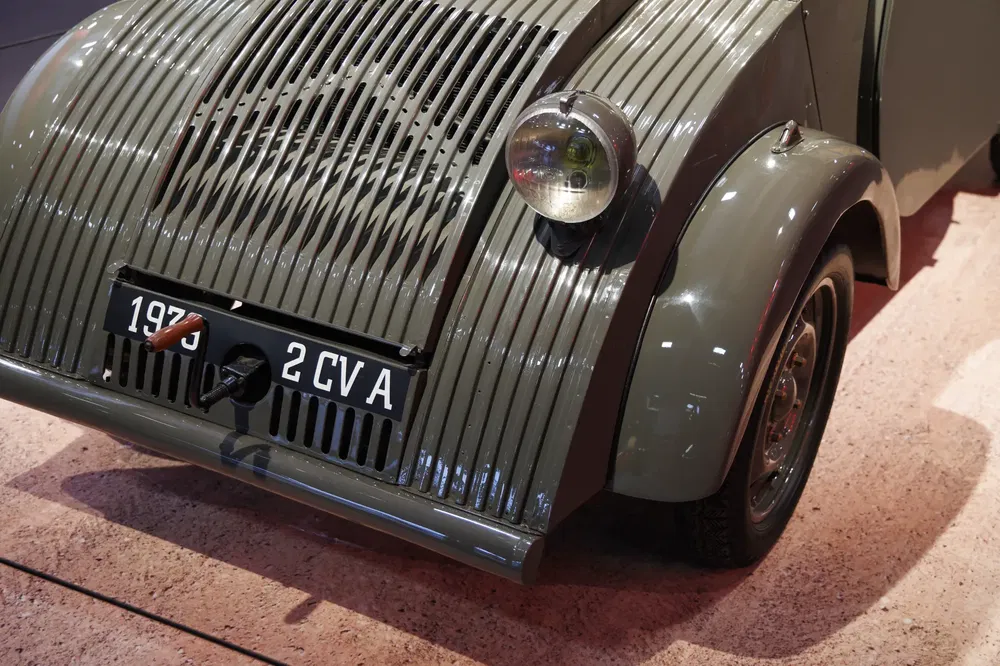 Citroën 2CV de 1939, grise, avec phares ronds et plaque d'immatriculation visible.