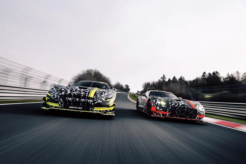 Deux Mercedes-AMG GT en camouflage sur circuit, vitesse élevée en courbe.