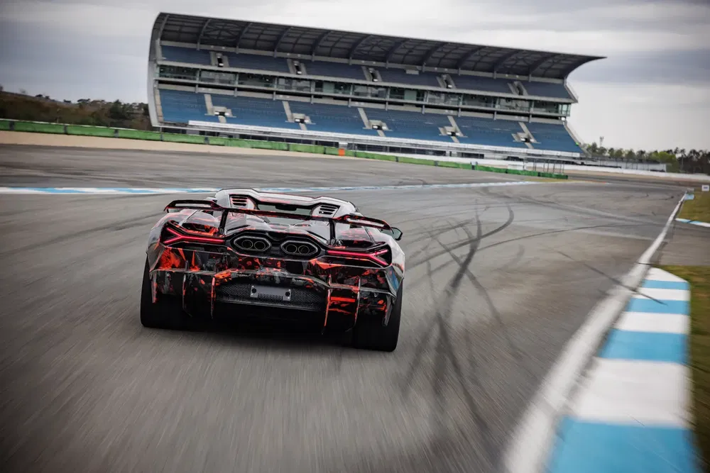 Lamborghini en camouflage sur circuit de course, arrière-plan tribune vide.