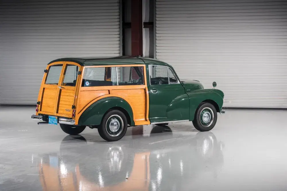 Voiture Morris Minor Traveller verte avec panneaux en bois, stationnée dans un garage moderne.