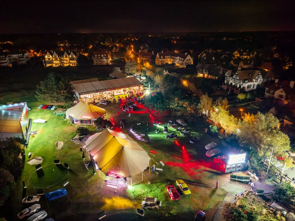Vue aérienne d'une exposition nocturne de voitures illuminées sous des tentes à proximité de maisons.