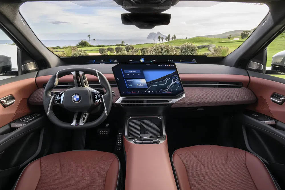 Modern interieur van BMW iX met digitaal dashboard en uitzicht op het landschap.