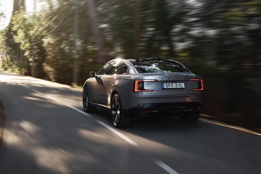 Voiture Volvo S90 grise roulant sur une route bordée d'arbres au crépuscule.