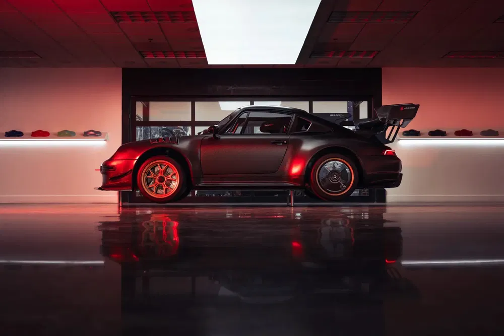 Porsche 911 noire avec éclairage rouge, exposée dans un showroom moderne.