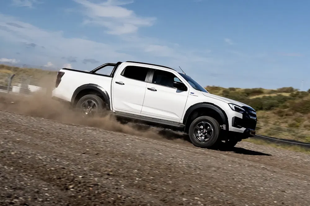 Pickup Isuzu D-Max blanc roulant sur un chemin de terre, ciel bleu en arrière-plan.