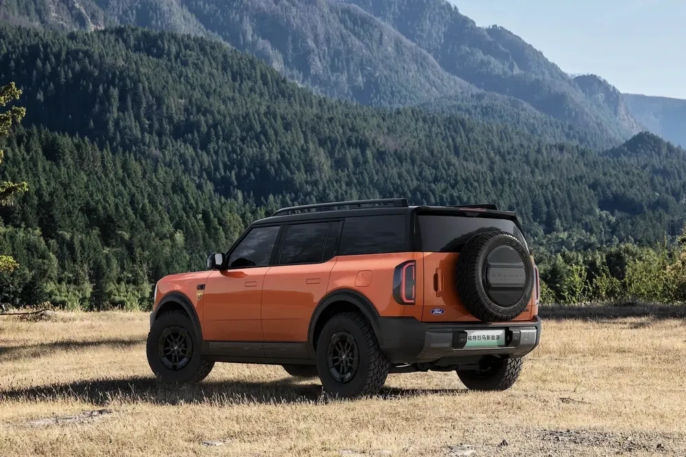 Ford Bronco orange stationné dans un paysage montagneux boisé majestueux.