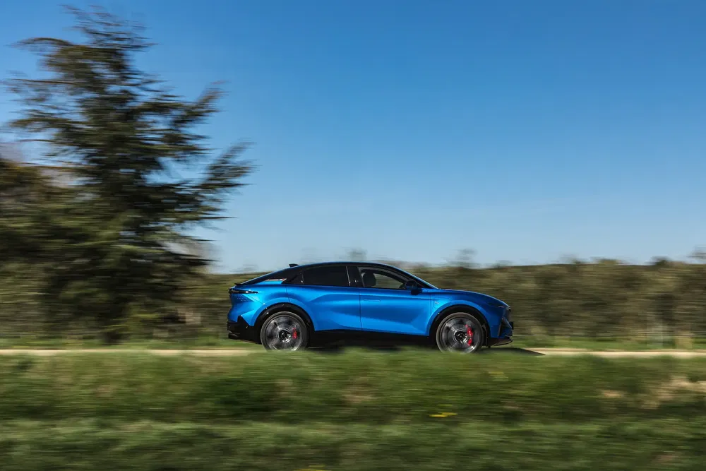 Blauwe Ford Mustang Mach-E elektrische auto rijdt in een natuurlijke omgeving.